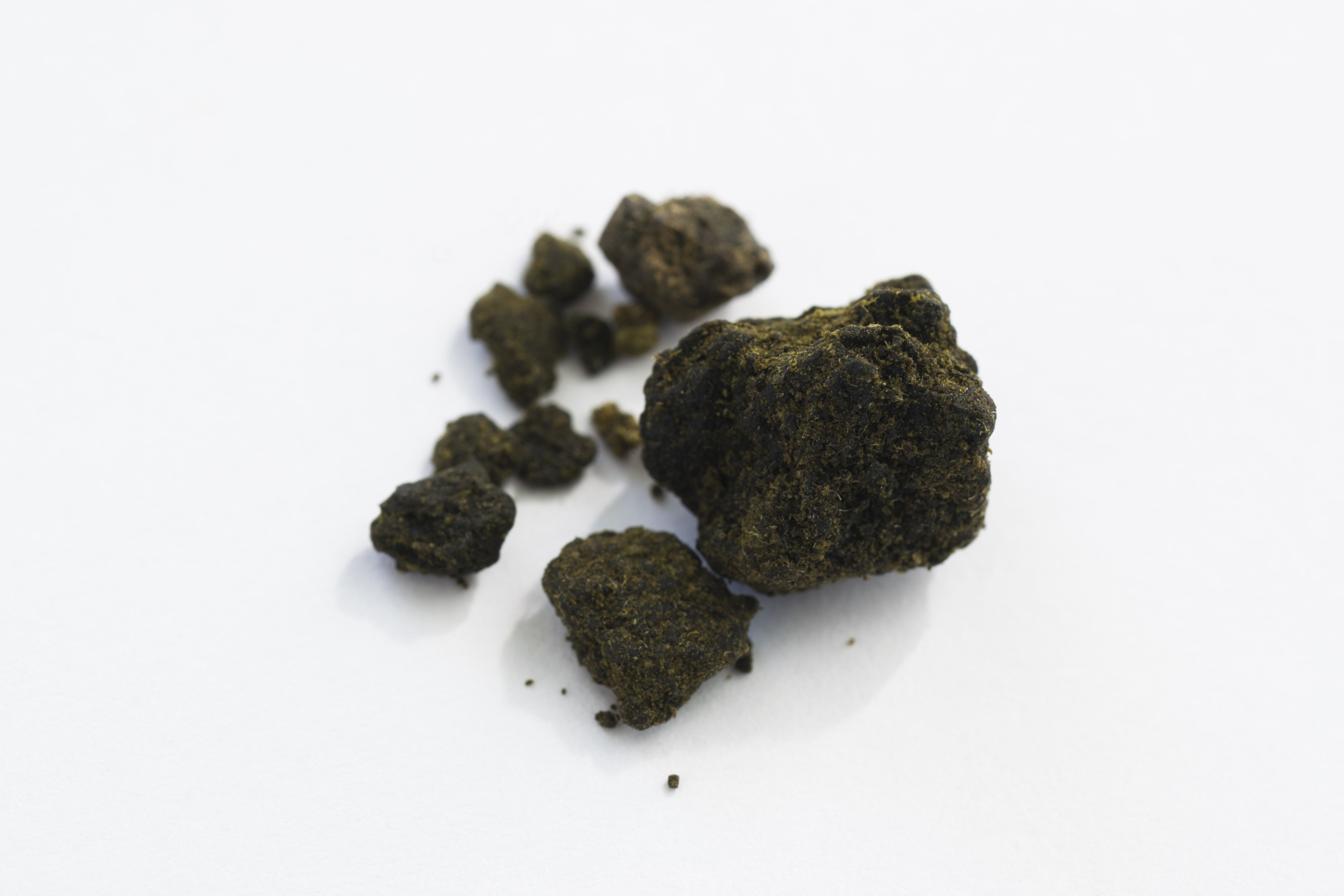 Chunks of broken dark brown and green hashish sit on a white background.