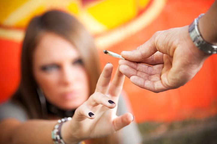 Man handing a joint to a woman sitting down.