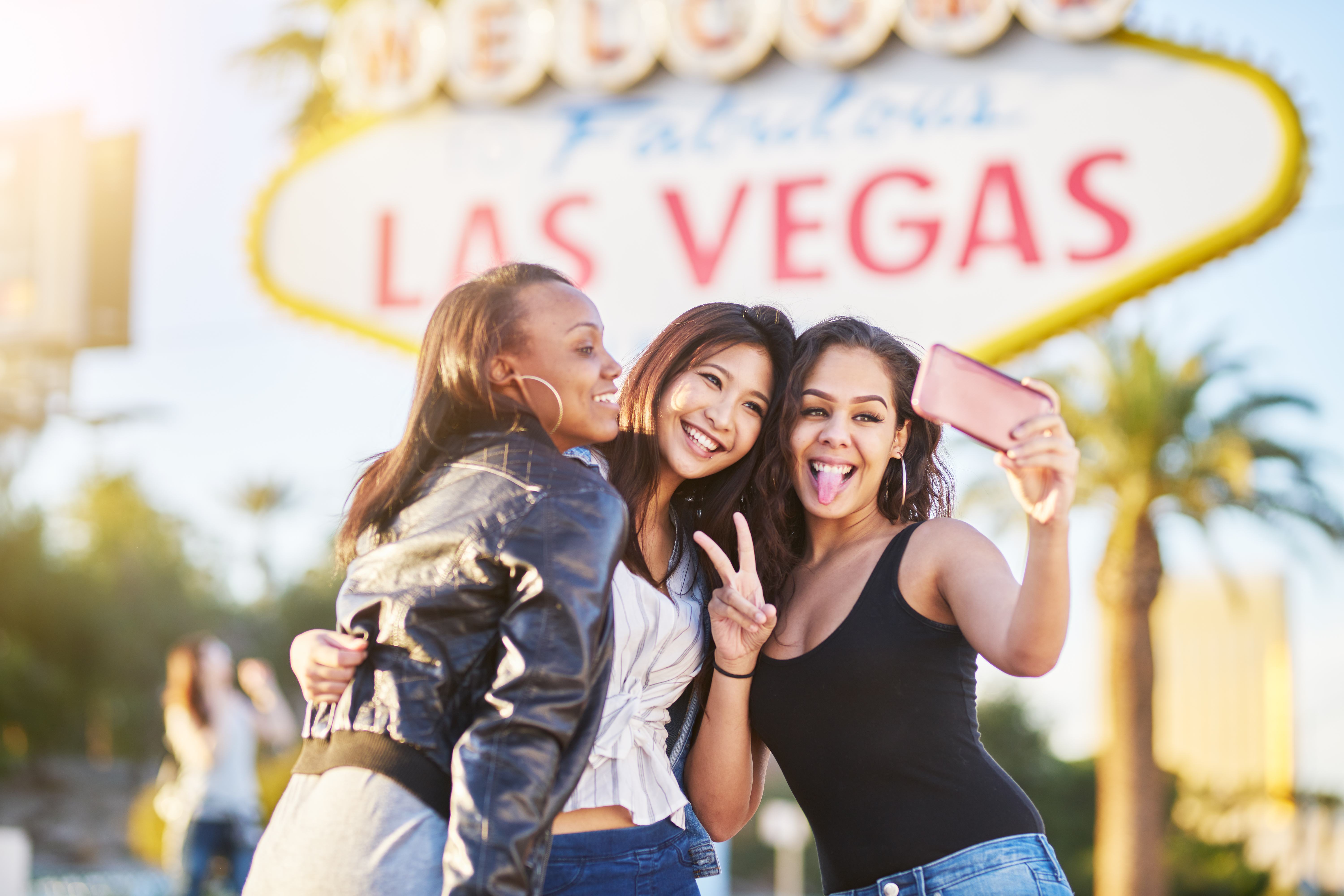 3 women taking a group selfie photo in front of the Las Vegas sign.